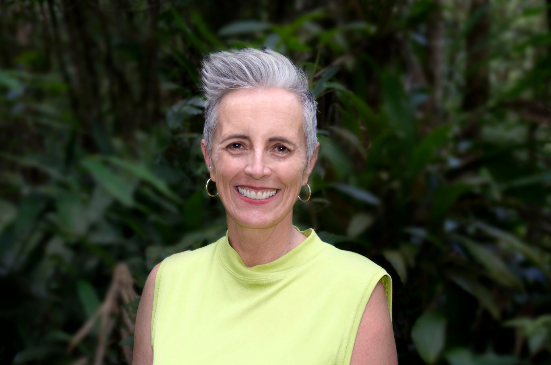 Portrait of Jen, education consultant and former Principal, smiling in front of dense green foliage